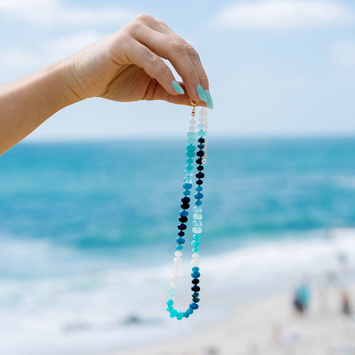 Blue Crush Statement Healing Necklace, held up over the sea