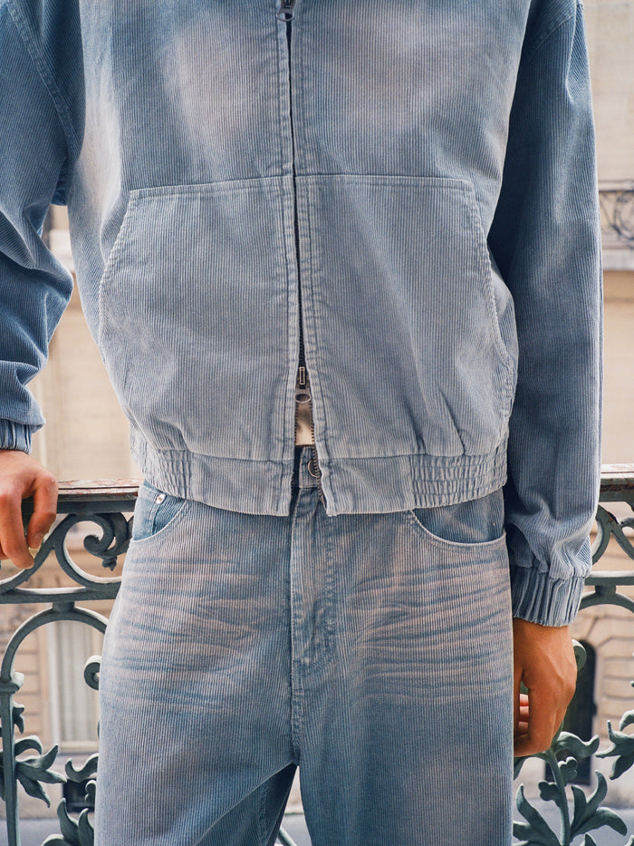 A person wearing FOUND Corduroy Flare Work Pants and a vintage blue corduroy jacket stands by a decorative metal railing, highlighting the pants' relaxed fit.