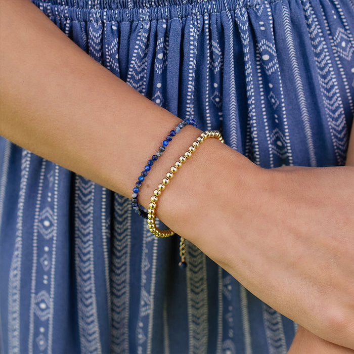 Gold 4mm Stretch Bead Bracelet, on wrist by a blue dress
