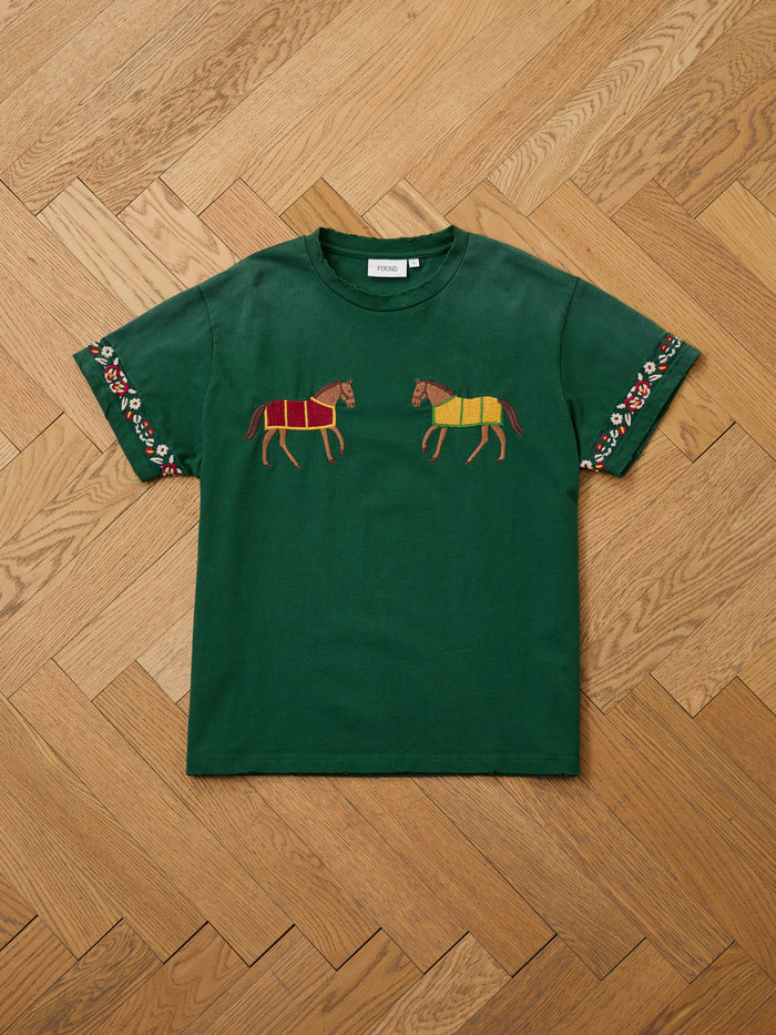 FOUND Horse Equine Tee: green short-sleeve shirt with embroidered horses on the chest and floral sleeve accents, shown laid flat on a herringbone wooden floor.