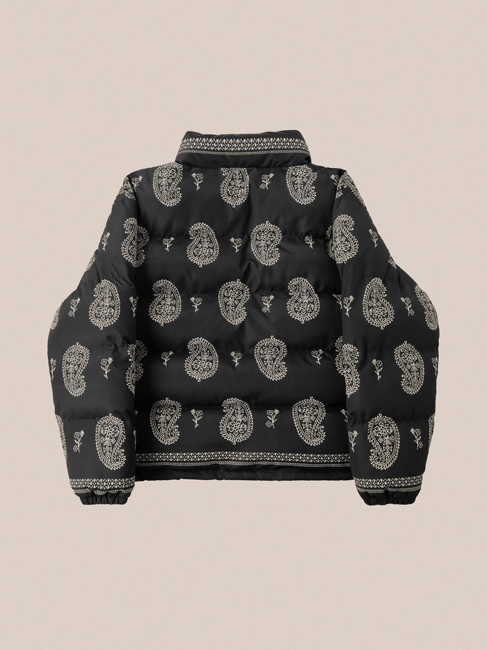 Back view of the Profound Paisley Puffer Jacket in Black, showcasing intricate white bandana paisley patterns set against a beige background, crafted with a sleek nylon shell.