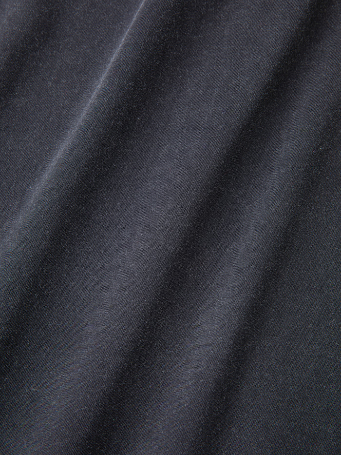 A close-up of the Stitched Border Distressed Logo Hoodie by FOUND, showcasing its smooth, dark grey fabric with diagonal folds and a soft texture that evokes the feel of vintage black French terry cotton.