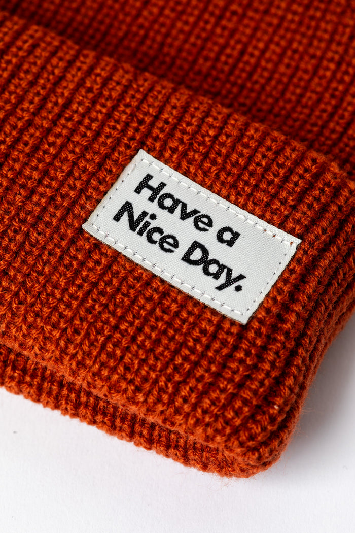 Detail of rust orange knit acrylic beanie with a "Have a Nice Day" patch