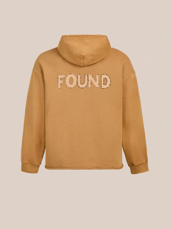 The Beadwork Logo Hoodie by FOUND is a tan vintage-style hoodie crafted from soft French terry cotton, with the brand's name boldly displayed across the back.