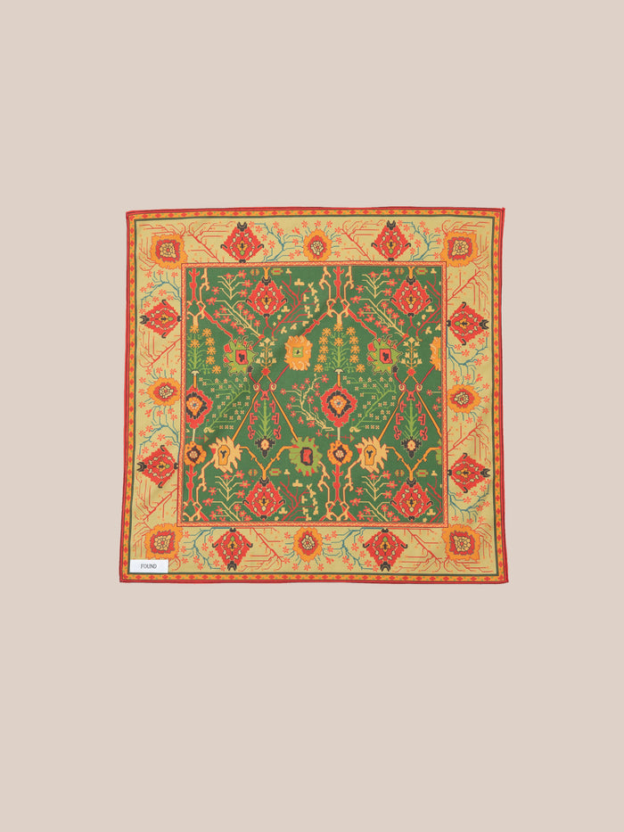 Discover the Botanical Mosaic Bandana by Found, a square scarf made from a soft cotton blend. It features an elaborate floral and geometric design in lively green, red, and yellow hues, inspired by intricate Indo-Aryan prints.