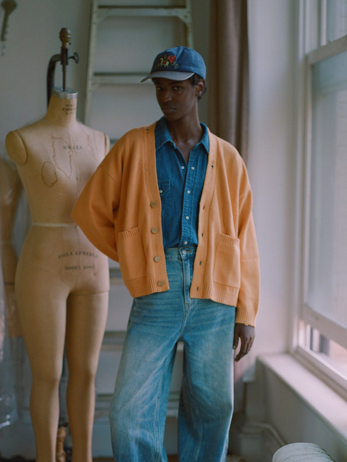 A man in a Cadmium Distressed Cardigan by Found with chunky ribbing standing next to a mannequin.