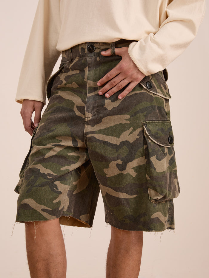 Model wears FOUND Camouflage Twill Utility Cargo Shorts and a light long-sleeve shirt, highlighting the unisex relaxed fit with one hand resting casually on the waistband.
