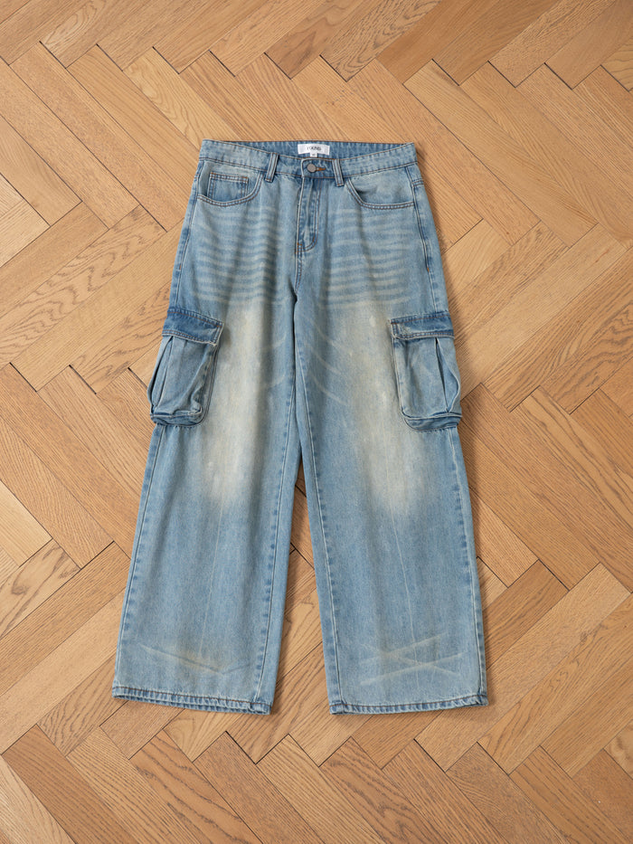 FOUND's wide-leg cargo jeans in blue, featuring a relaxed fit and utilitarian edge, are displayed flat on a wooden herringbone floor.