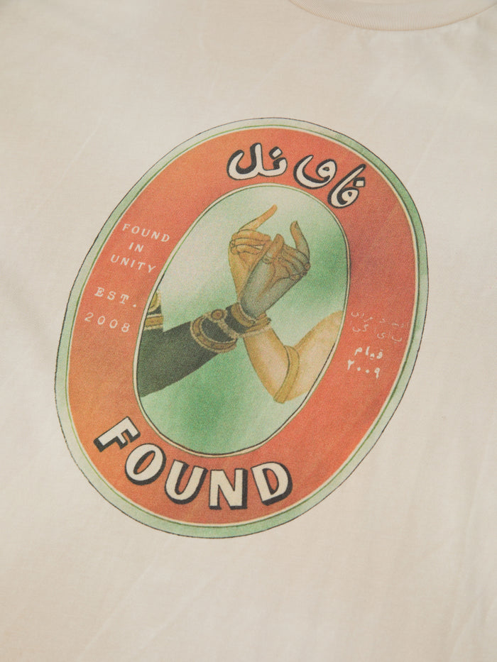 The FOUND Community Hands Tee features two hands reaching inside an oval, blending vintage matchbox art with English and Arabic text: "Found in Unity Est. 2008" and "FOUND." A unique t-shirt statement about unity.