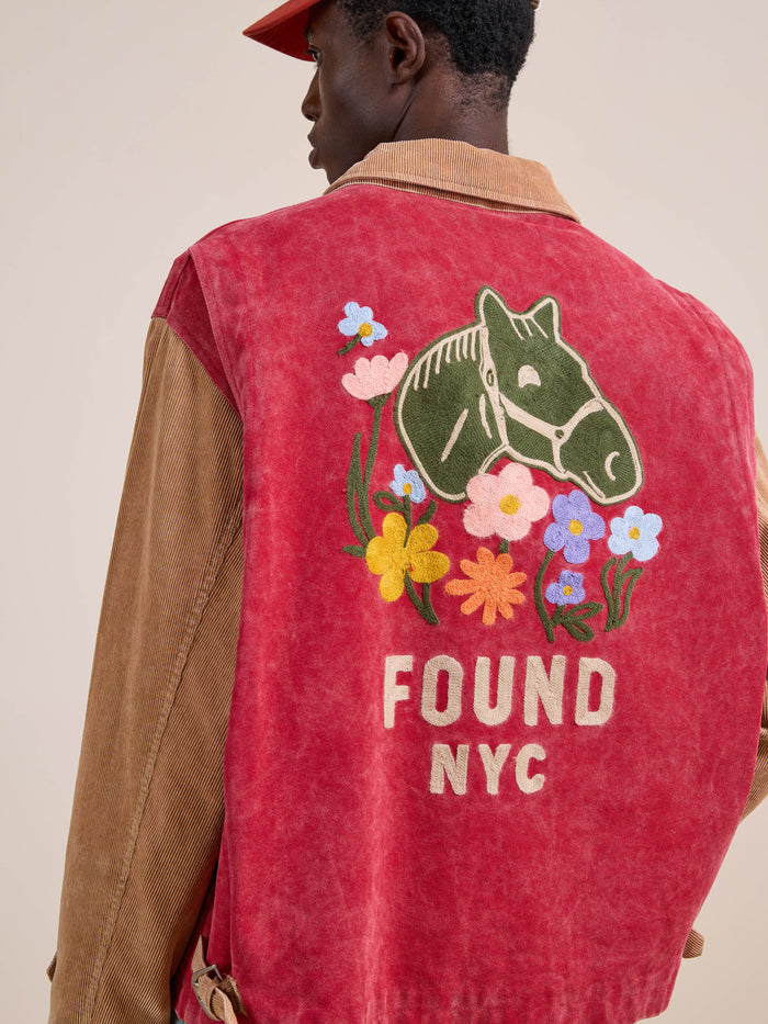 Someone wears the Found Corduroy Field Jacket, a unisex red and tan piece featuring a horse head and colorful flowers embroidered on the back, plus "FOUND NYC" text.