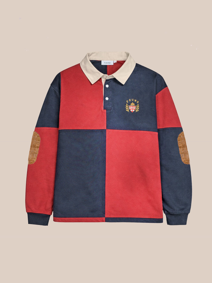 The FOUND Crestfield Rugby is a unisex relaxed fit shirt featuring red and navy color blocks, a beige collar, chest crest logo, and brown elbow patches, shown on a plain beige background.