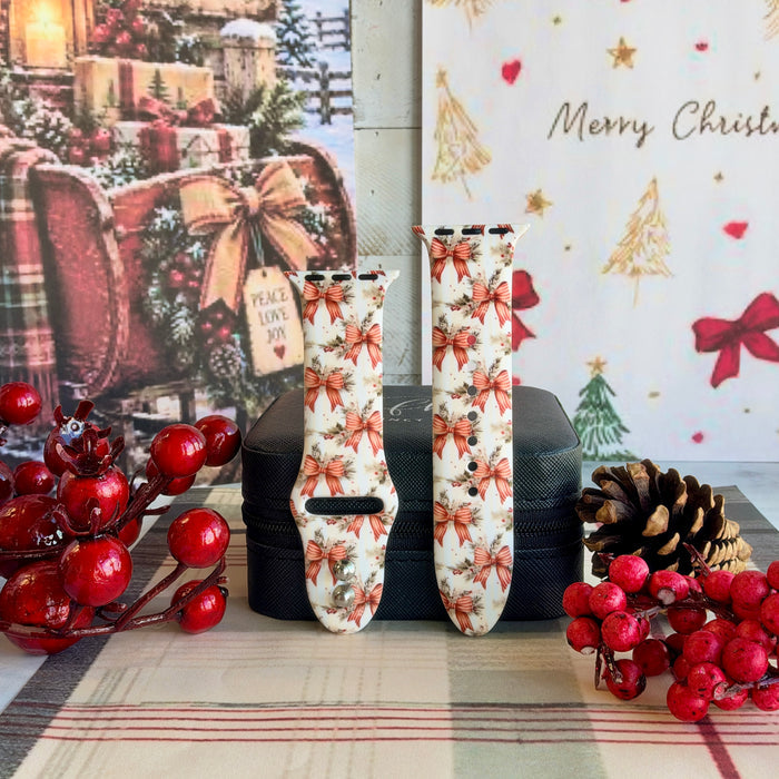 Both straps of the Deck The Halls With Bows & Holly silicone Apple Watch band on a black jewelry box with red berries and a pinecone
