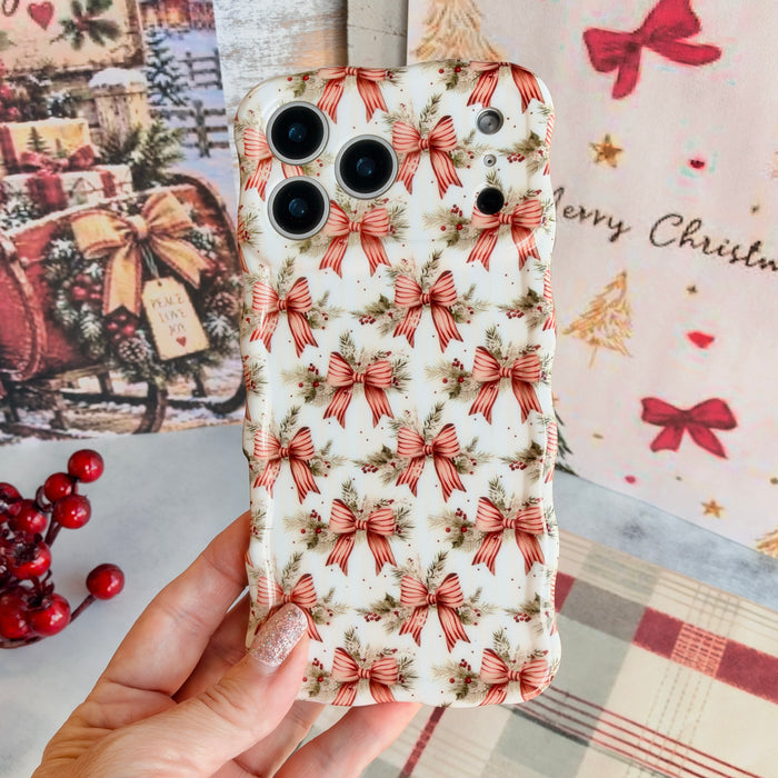 Hand holding the Deck The Halls With Bows & Holly Wavy Luxe MagSafe iPhone case, striped red ribbon bows with pine and holly on ivory, beside vintage sleigh art and plaid