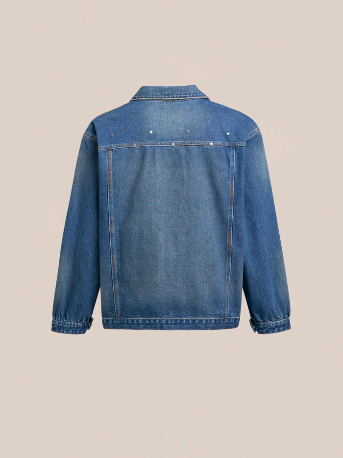 The FOUND Denim Carpenter Jacket features a back view with a collar and long sleeves in blue denim, set against a beige background. This unisex piece offers a relaxed fit, making it an essential workwear staple for any wardrobe.