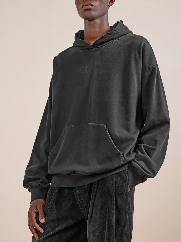 A person in the FOUND Distressed Pullover Hoodie and black corduroy pants stands against a plain light background.
