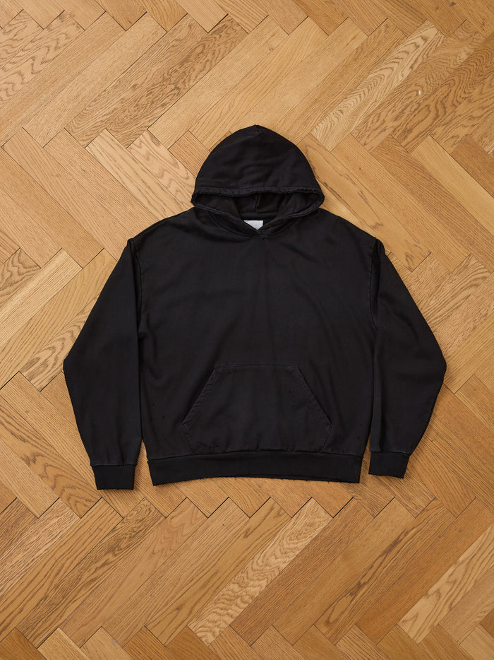 The FOUND Distressed Pullover Hoodie, featuring a front pocket and classic unisex relaxed fit, is displayed flat on a wooden parquet floor, highlighting its timeless vintage style.