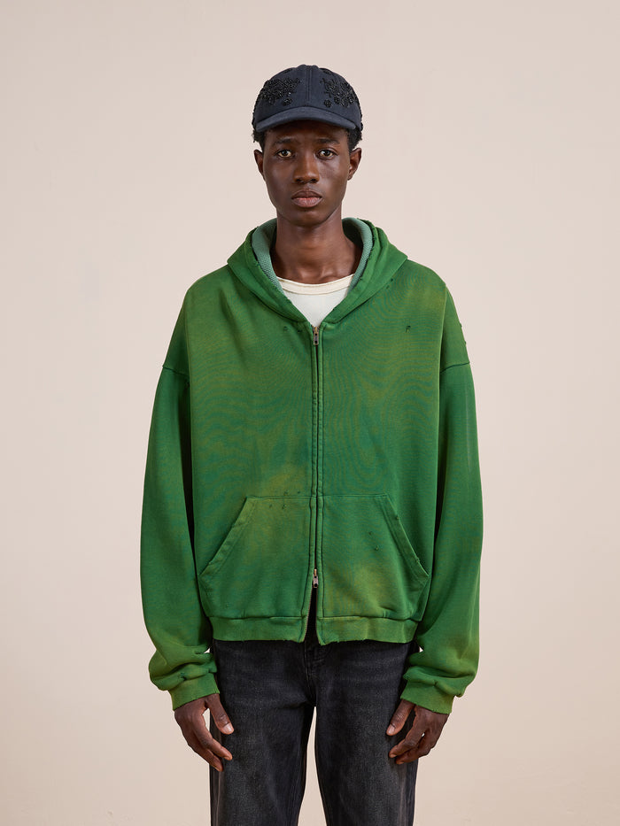 A person in a FOUND Distressed Thermal Lined Zip Up Hoodie, white shirt, dark jeans, and a dark cap stands against a plain beige background.
