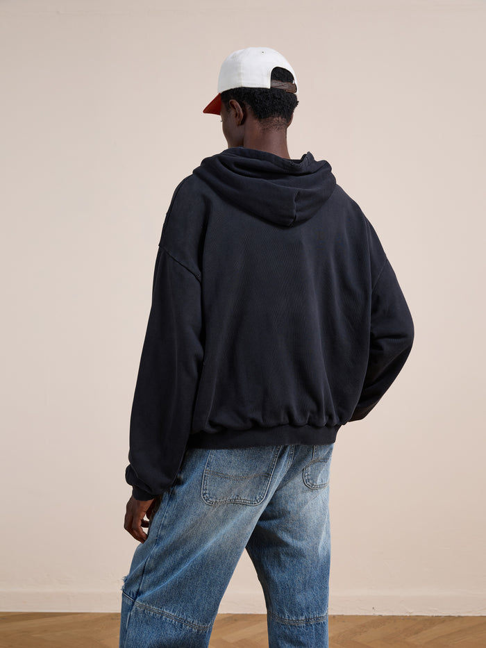 Someone wearing the FOUND Distressed Thermal Lined Zip Up Hoodie in black, blue jeans, and a two-tone baseball cap stands facing away from the camera in a neutral indoor setting.