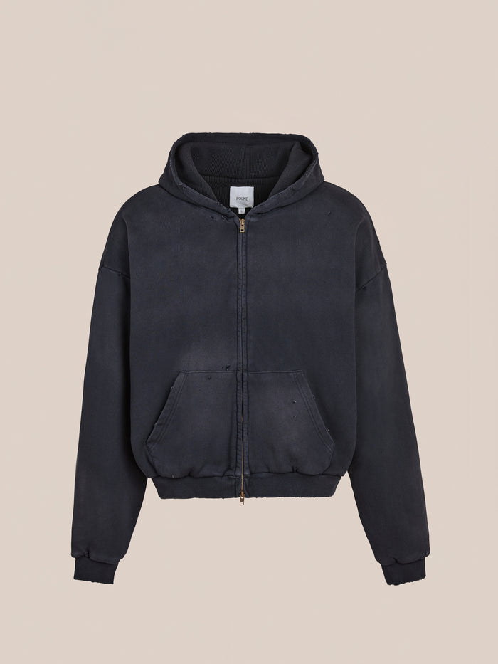 The FOUND Distressed Thermal Lined Zip Up Hoodie is a black unisex relaxed-fit hoodie featuring a hood, front pouch pockets, and ribbed cuffs and hem, shown against a plain beige background.