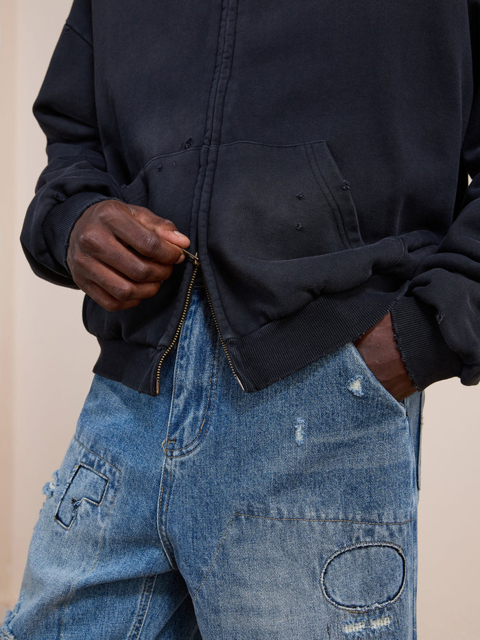 A person wearing the FOUND Distressed Thermal Lined Zip Up Hoodie and distressed blue jeans with patchwork detail holds the hoodie zipper.