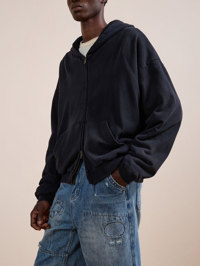 A person wearing the FOUND Distressed Thermal Lined Zip Up Hoodie in black over a white t-shirt and blue distressed jeans, standing with one hand in their pocket.