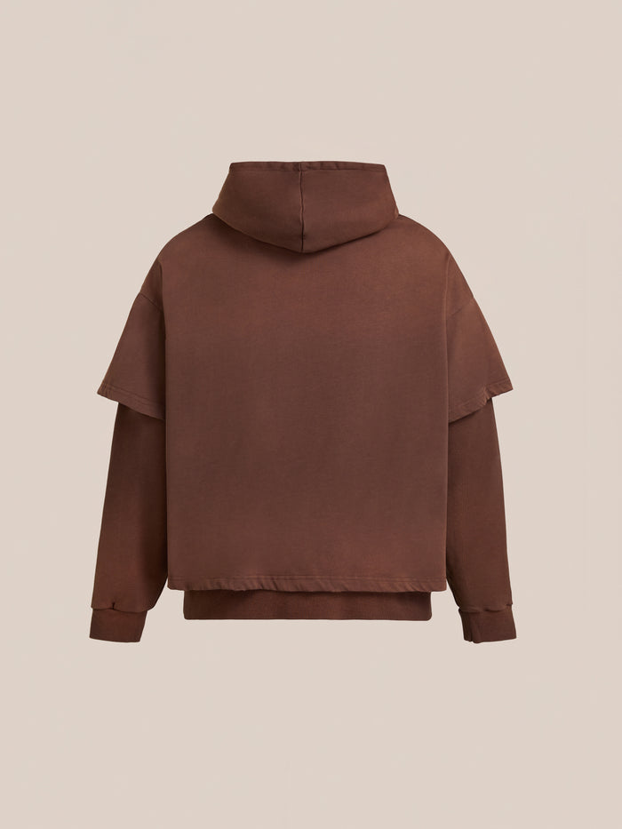 Back view of the Found Double Layer Hoodie, featuring a brown vintage look, dropped shoulders, and long sleeves in french terry cotton. Displayed against a plain beige background.