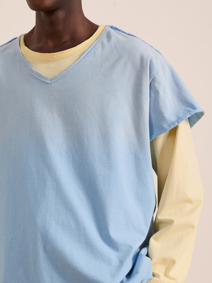 A person wears a light blue FOUND Double Layer LS Tee with sunfade wash over a pale yellow long-sleeve shirt. The head is partially cropped out of the image.