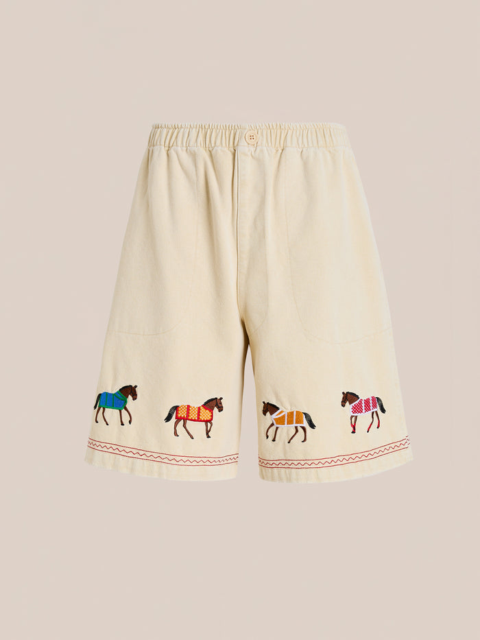 The Profound Embroidered Horse Shorts are beige cotton twill shorts with an elastic waistband, front pockets, and colorful embroidered horses along the hem.