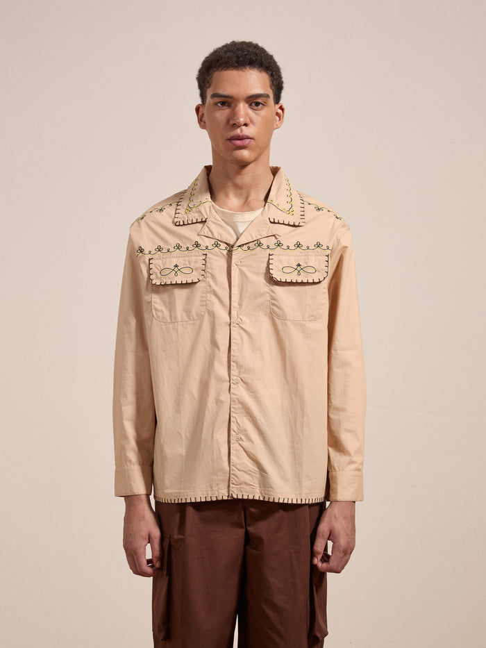 A person wearing the FOUND Embroidered Western Button Up in light beige with decorative stitching and dark brown pants, standing against a plain background.