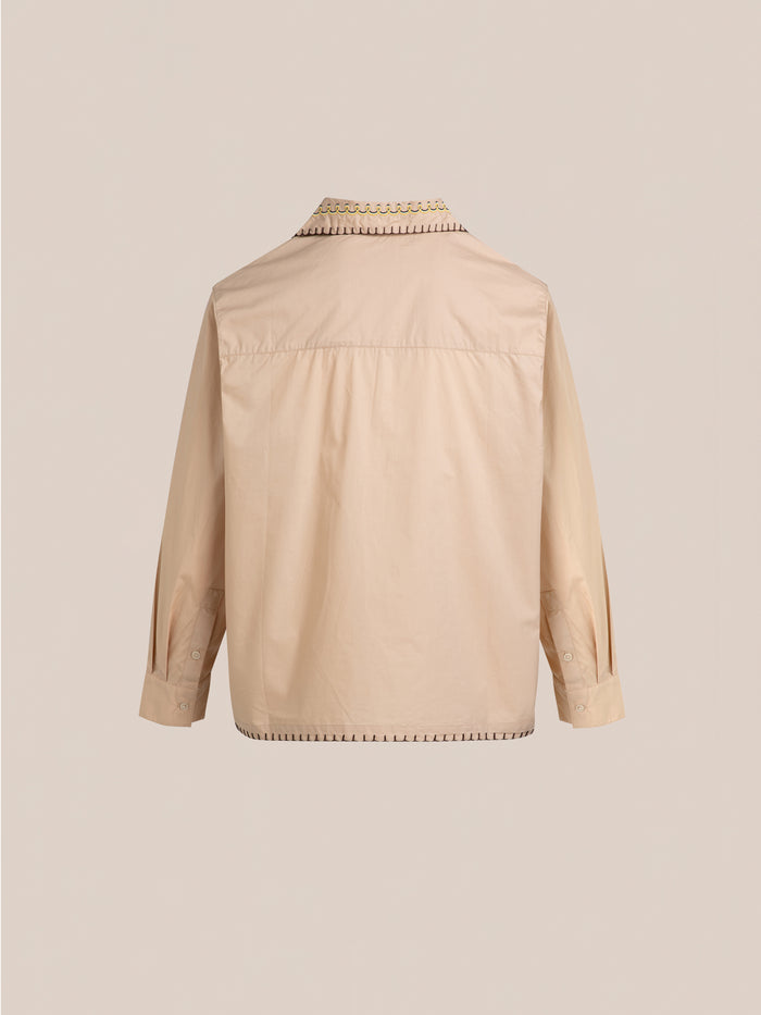 FOUND's Embroidered Western Button Up in beige is shown from the back, highlighting its buttoned cuffs, shoulder pleats, and intricate stitching along the collar and seams.