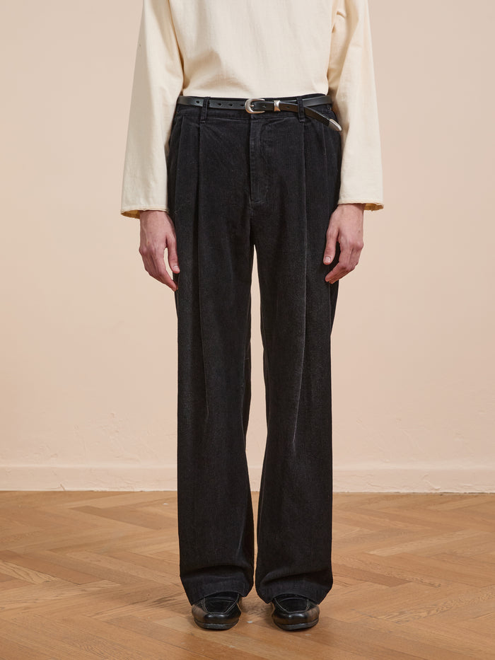 Person wearing a cream long-sleeve shirt, FOUND Faded Pleated Corduroy Pants with a belt, and black shoes, standing on a wooden floor against a beige wall.