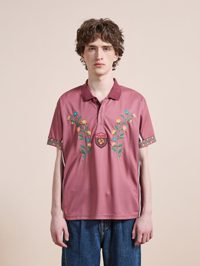 A person poses against a neutral background wearing the FOUND Floral Polo Jersey with botanical embroidery, a "FOUND" crest, and blue jeans.
