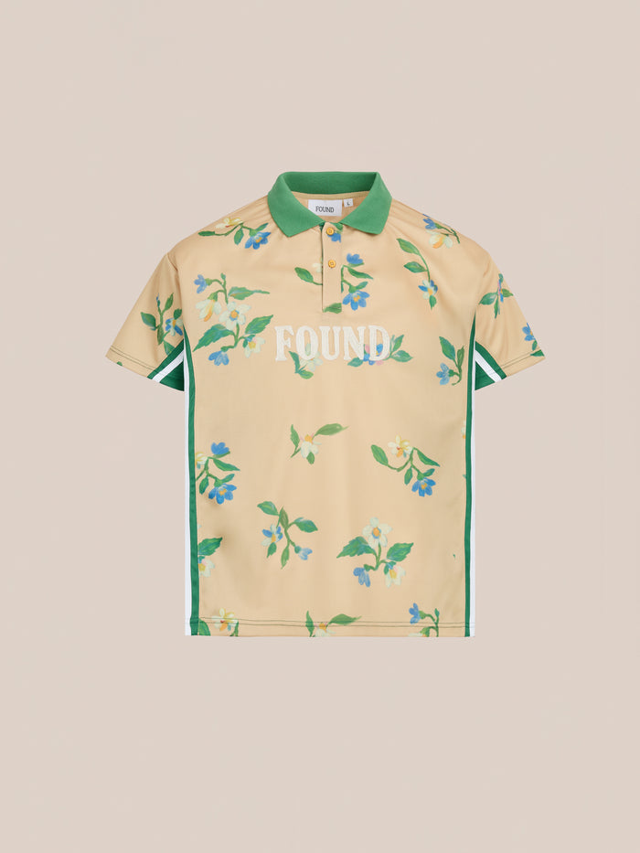 The FOUND Floral Polo Jersey is a beige unisex polo with green floral print, green collar lining, side stripes, and "FOUND" in white on the front. Relaxed fit inspired by vintage sporting shirts for a timeless style.