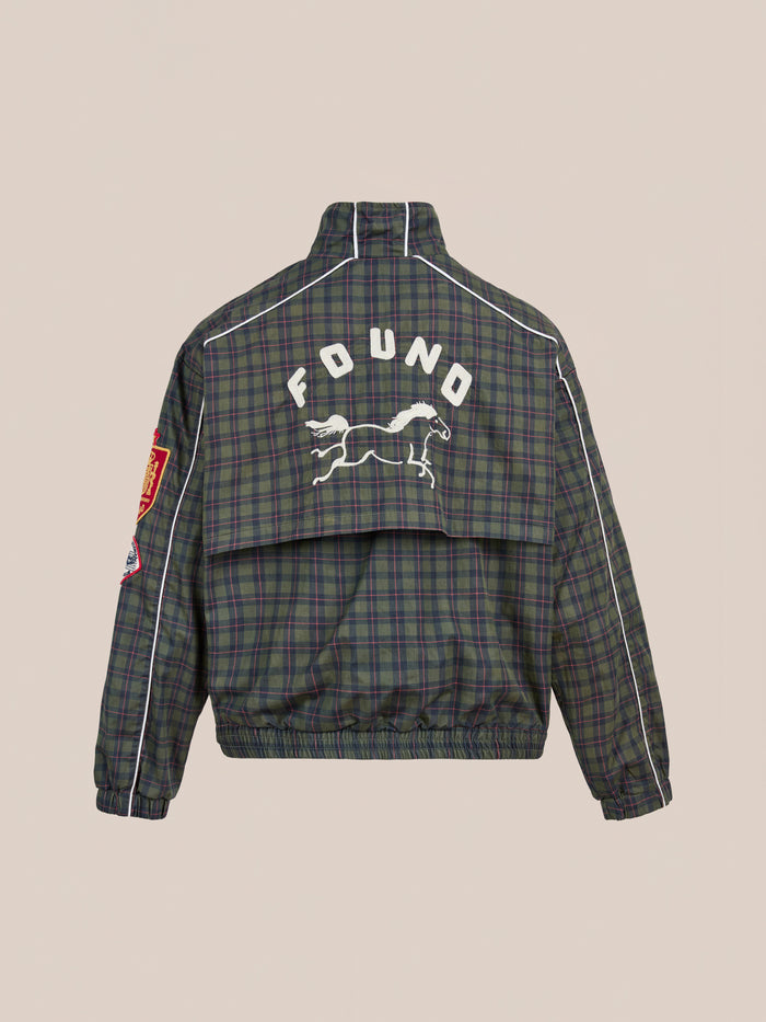 The FOUND Forest Plaid Track Jacket features green and navy plaid with white piping, a red sleeve patch, and a leaping animal graphic plus "FOUND" on the back—a lightweight cotton jacket inspired by vintage sport style.