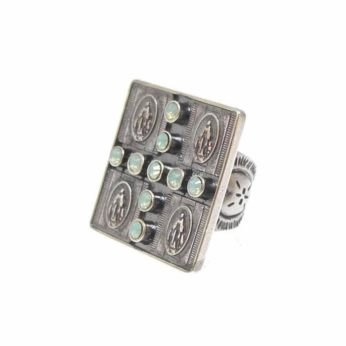 Square statement ring featuring a cross pattern of pale green stones, set against an antique silver-toned band with religious medallions.