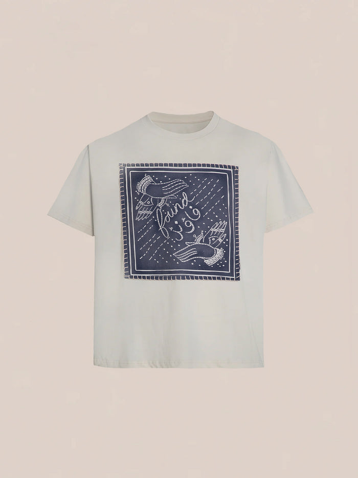 The Hand Art Graphic Tee from FOUND showcases a blue square graphic with birds and the word "found," drawing inspiration from Mughal paintings. Made from soft cotton twill, this white T-shirt adds artistic elegance and comfort to your wardrobe.