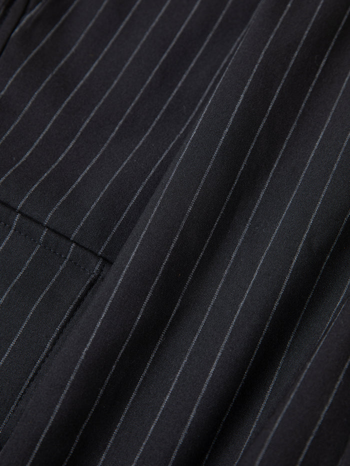 Close-up of black fabric with thin white pinstripes and a pocket, highlighting FOUND's Hava Pinstripe Pleated Cargo Trouser Shorts—stylish unisex design with an adjustable fit.