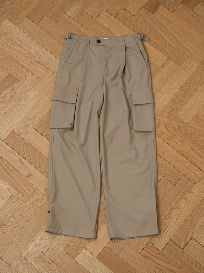 FOUND's Hava Pleated Cargo Trousers, made from durable cotton twill, lie flat on a herringbone wooden floor, showing off their utilitarian style and multiple pockets.