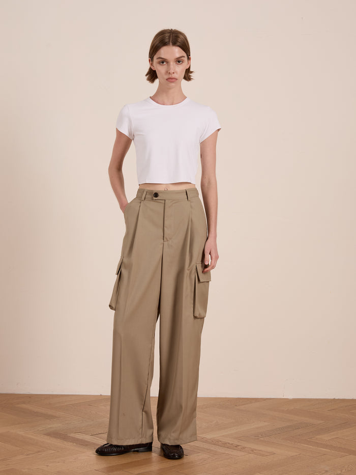 A person in a white cotton blend crop top and Hava Pleated Cargo Trousers by FOUND stands on a wooden floor against a plain background, embodying utilitarian style.