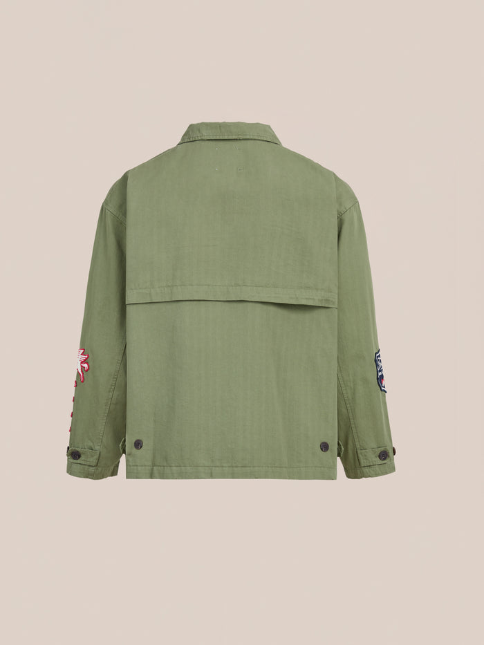 The FOUND Herringbone Utility Patchwork Jacket is shown from the back, featuring buttoned cuffs and hem, with embroidered sleeve patches and crafted from durable cotton herringbone.