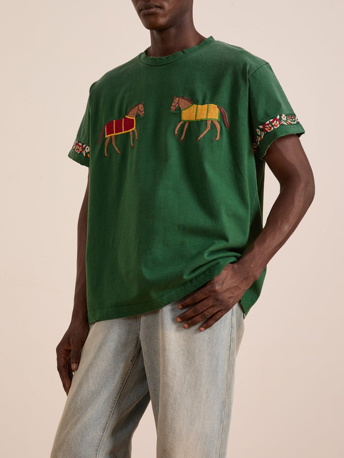 A person wears the FOUND Horse Equine Tee featuring embroidered horses and floral sleeve patterns, paired with light blue jeans.