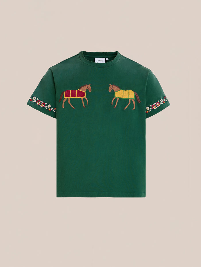 The FOUND Horse Equine Tee is a green short-sleeve shirt featuring embroidered horses on the chest and floral embroidery on the sleeves, shown against a plain beige background.
