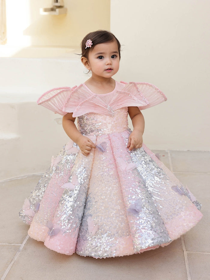 A pink shaded sequin gown with a wired neckline, pearl detailing, and butterfly accents‰ÛÓperfect for birthdays, carnivals, and special celebrations.