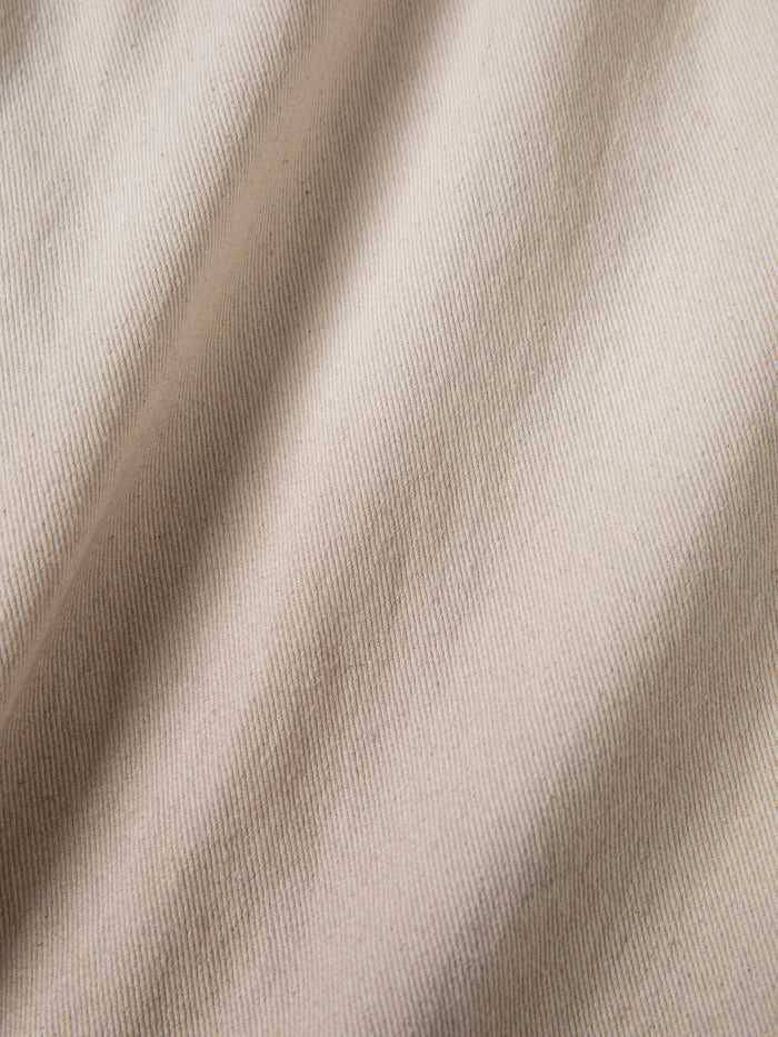 Close-up of FOUND Lacy Jean Jorts in beige, featuring a visible diagonal weave pattern like distressed denim and soft shadows that emphasize the textured fabric.