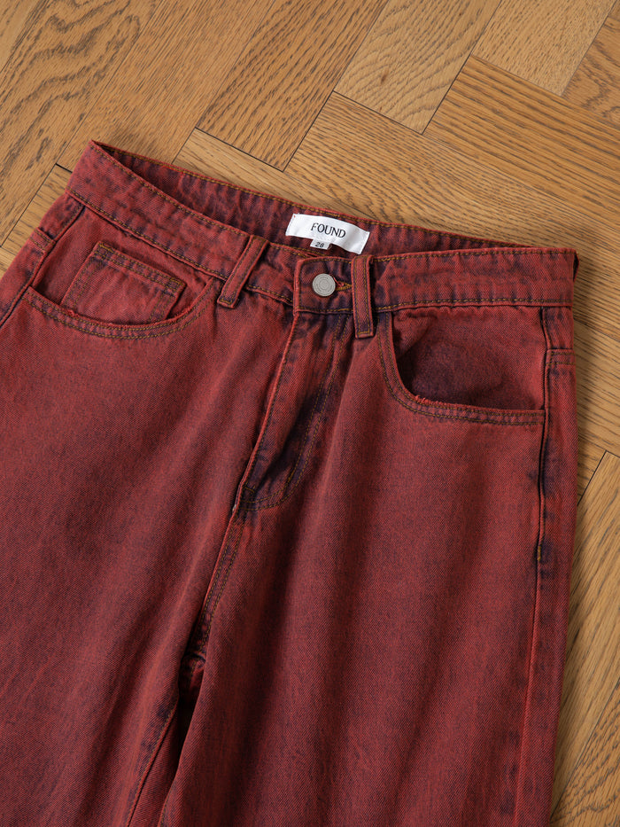 A pair of FOUND Lacy Jean Jorts in red acid wash, shown on a light wood parquet floor—ideal for making a bold unisex fashion statement.