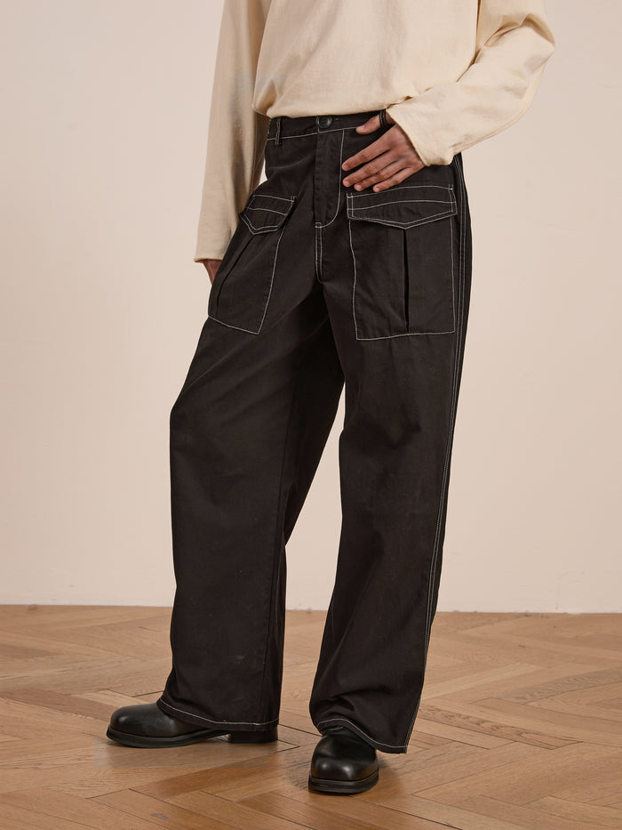 A person stands on wooden flooring, wearing a beige top with FOUND's Lucca Black Contrast Pocket Pants, which feature a relaxed straight-leg design made from midweight cotton twill.