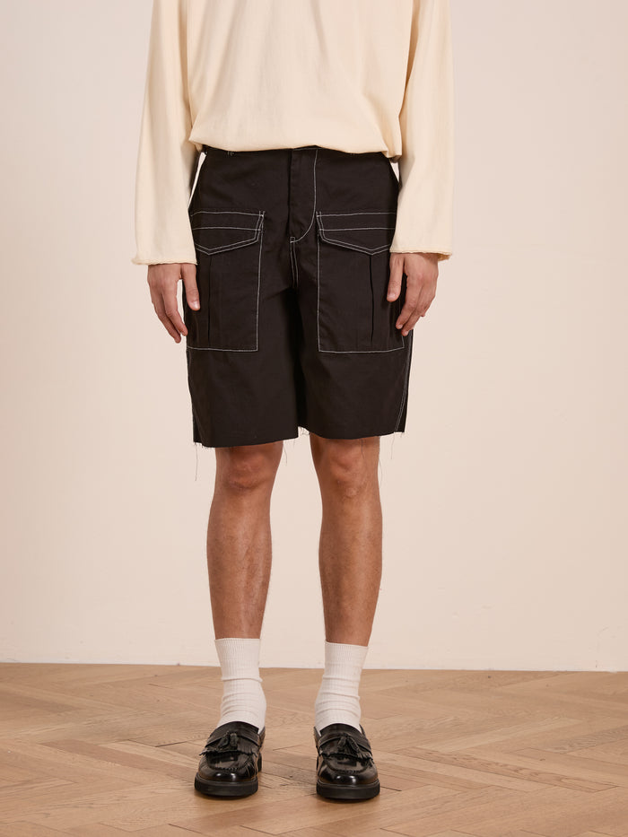 A person wearing a cream long-sleeve shirt, FOUND Lucca Black Contrast Pocket Trouser Shorts, white socks, and black loafers stands on a wooden floor.