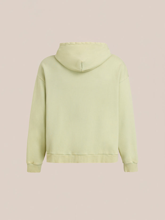The FOUND Motif Zip-Up Hoodie in light yellow is displayed from the back against a neutral beige background, highlighting its understated streetwear style.