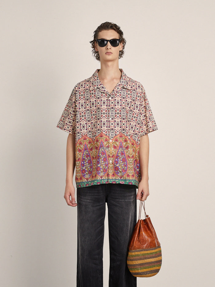 Person wearing sunglasses, the FOUND Mughal Camp Shirt, dark wide-leg pants, and holding a striped bag stands against a plain light background.