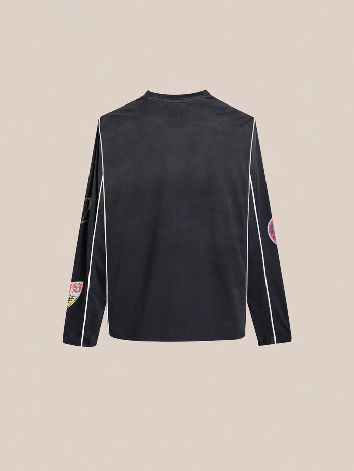 The FOUND Multi Language LS Jersey is a long-sleeve black football shirt with white piping and multicolored patches on the sleeves and shoulders, offering a retro silhouette ideal for unisex casual wear.